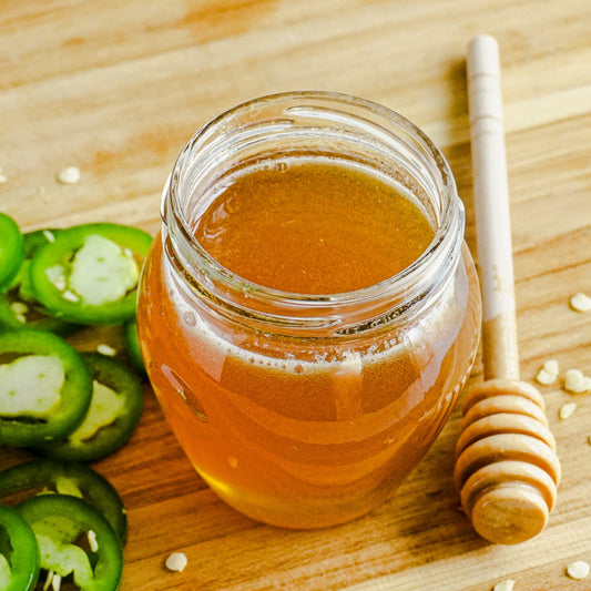 Hot honey in a glass jar next to jalapeños and honey sticks.