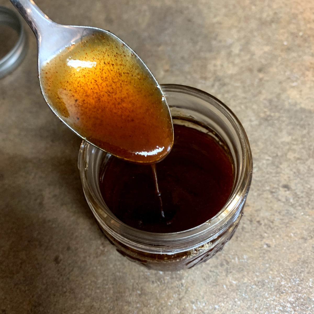 A spoon drizzling honey chipotle sauce into a jar.