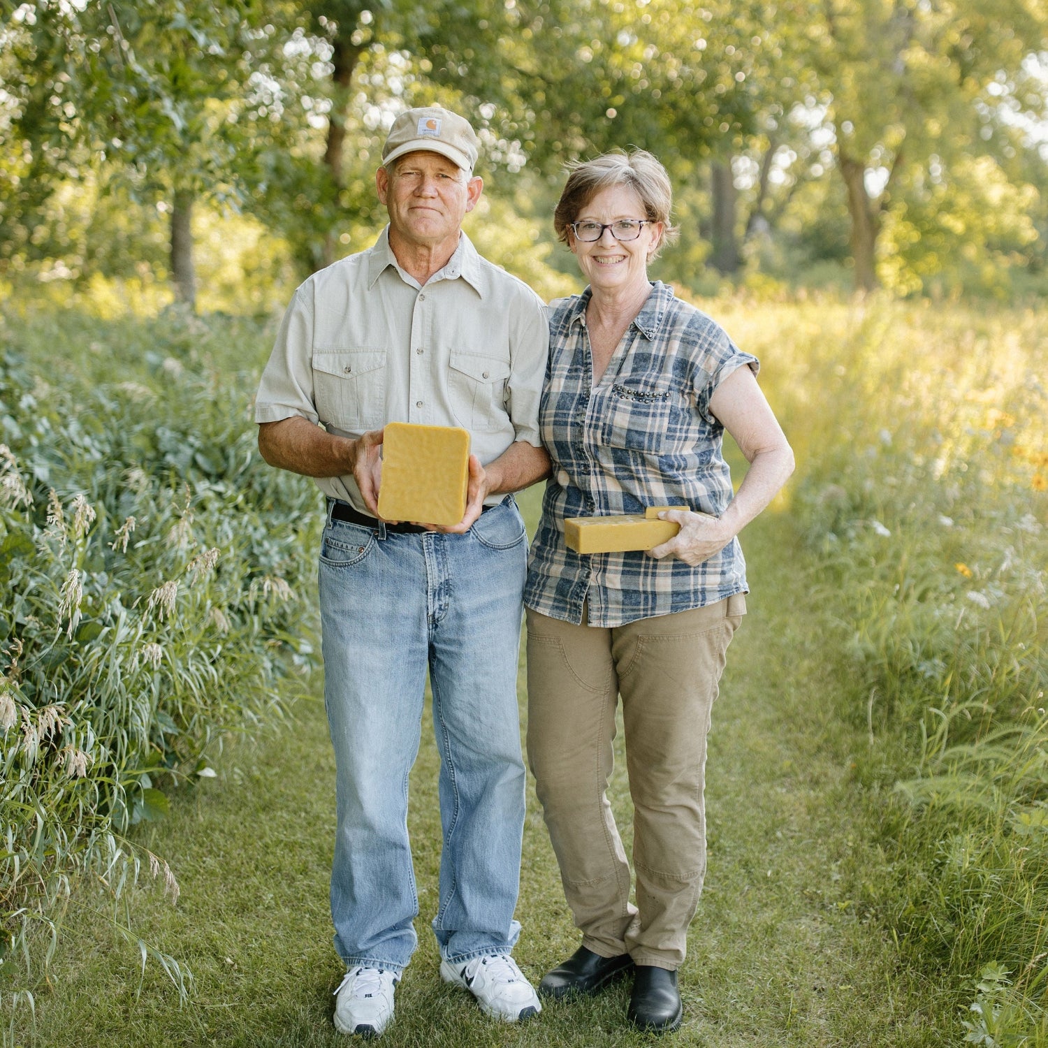 Mark and Becca standing in a field holding yellow beeswax.