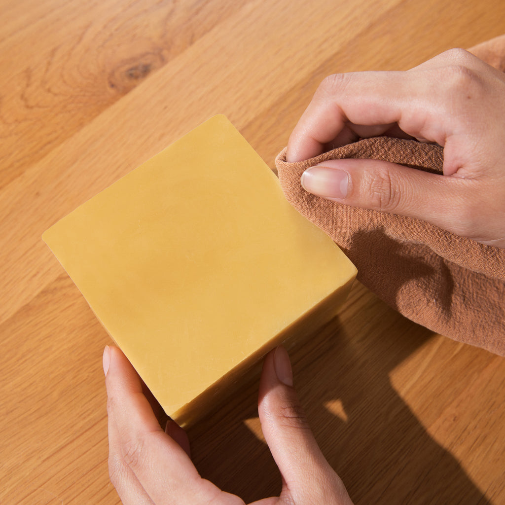 Person cleaning a beeswax block with a brown cloth.