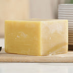 Block of yellow beeswax on a wooden surface with a neutral background
