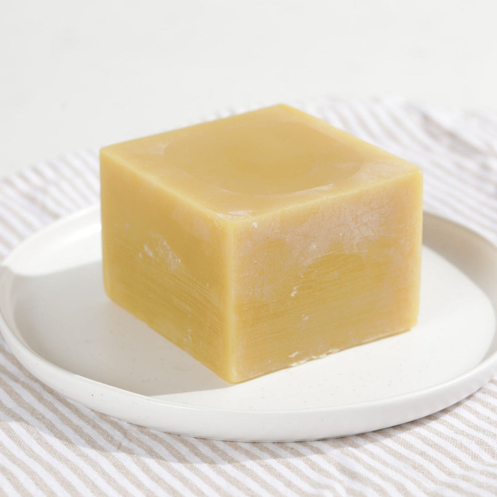 Square block of yellow beeswax on a white plate with a striped fabric background