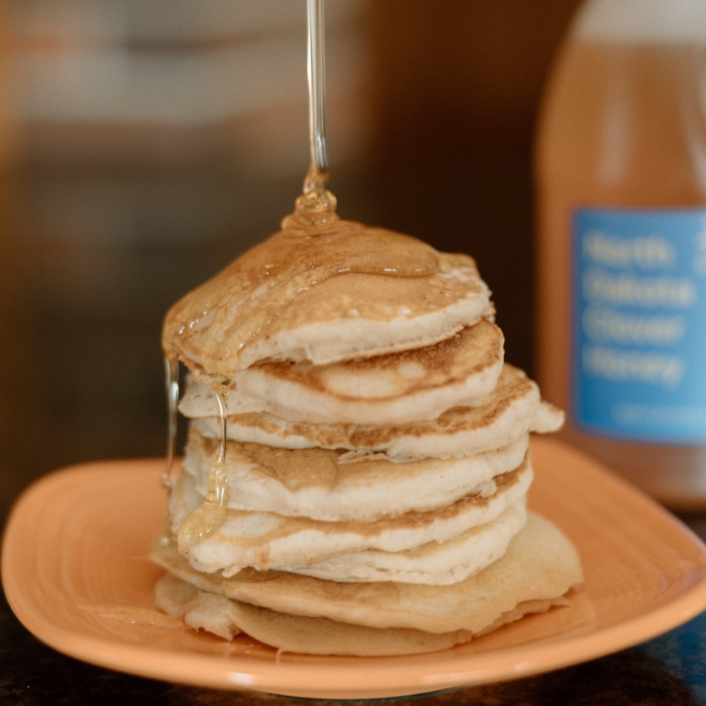 Clover honey being drizzled over a plate of pancakes.