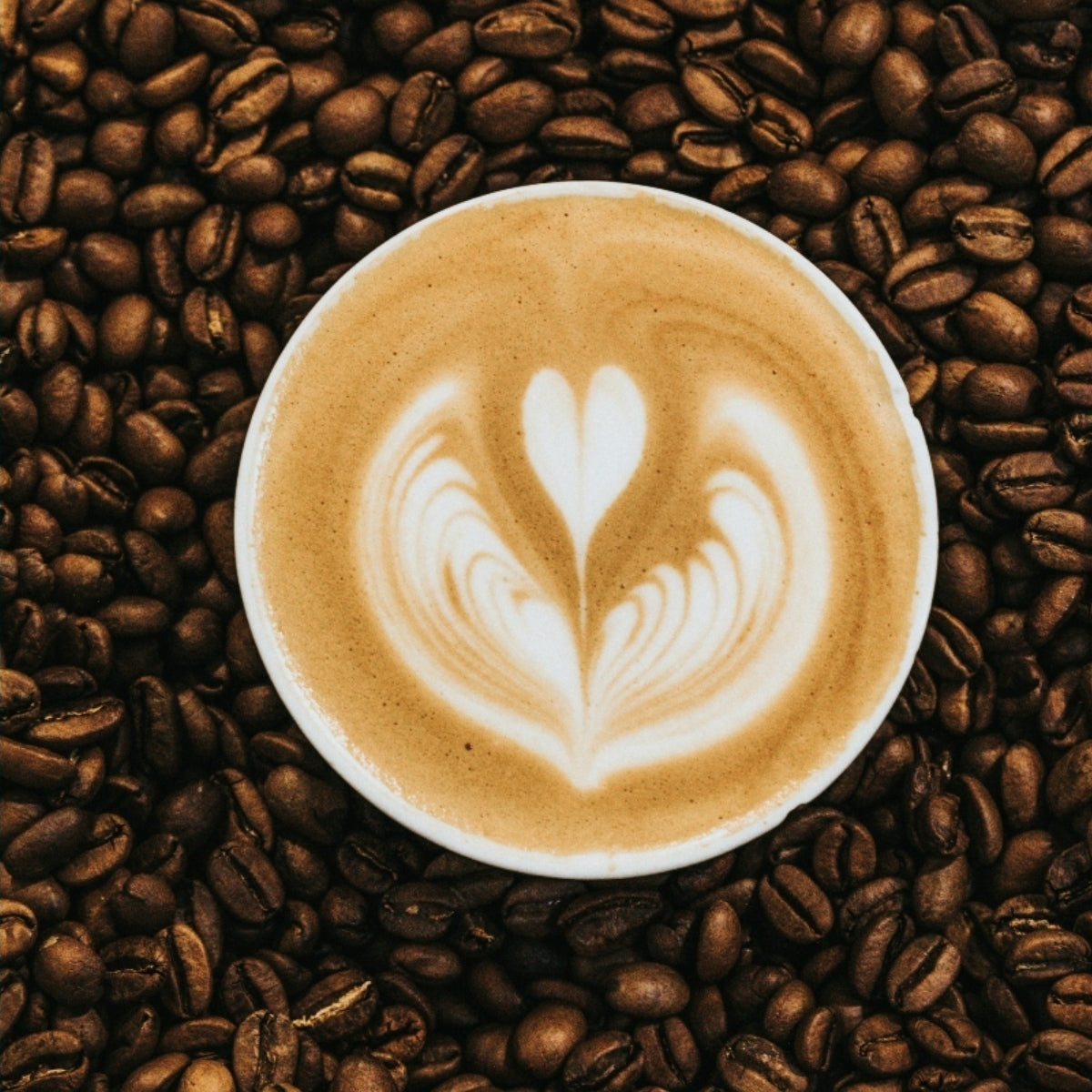 A latte that might contain honey, surrounded by coffee beans.