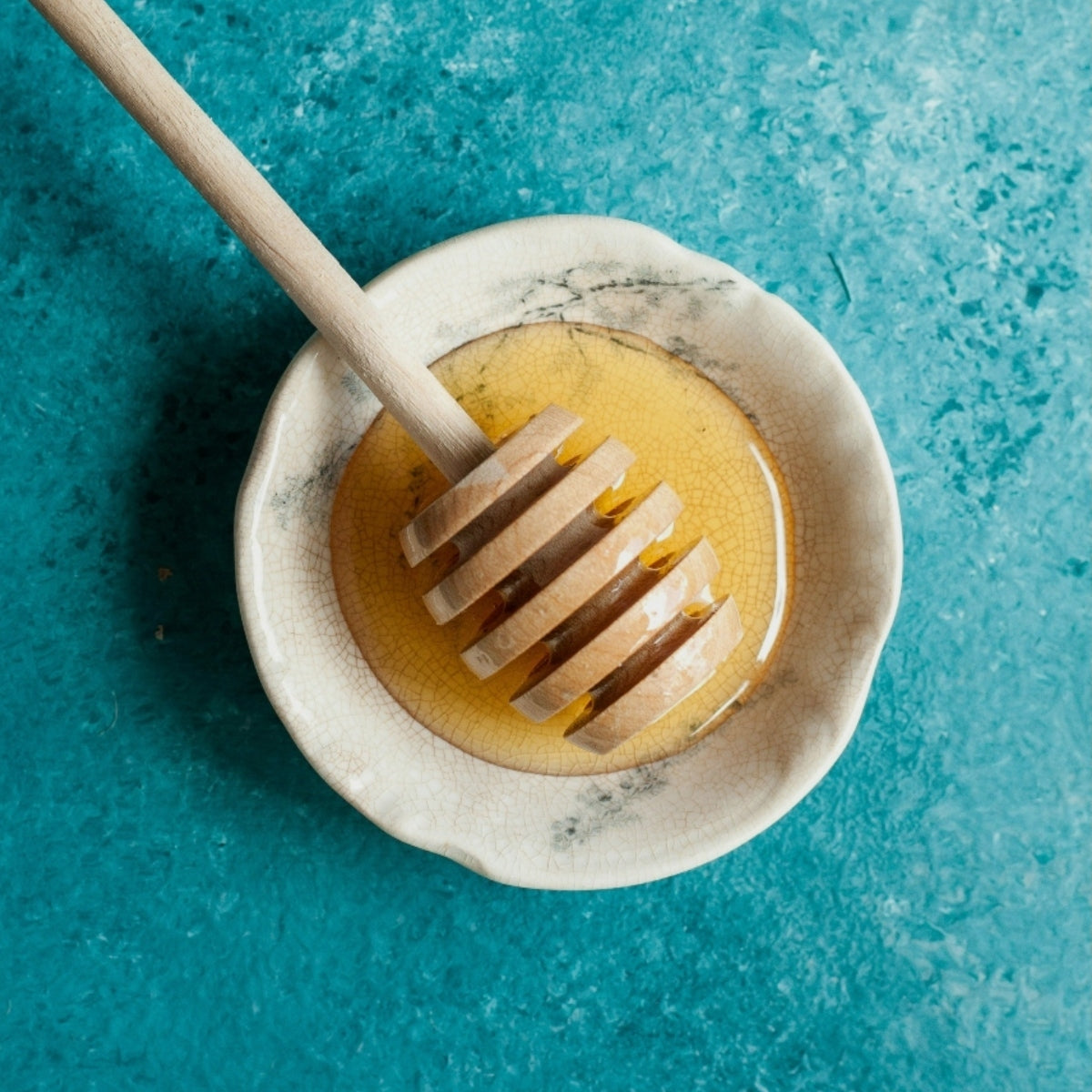 A honey stick in a bowl against a blue background.