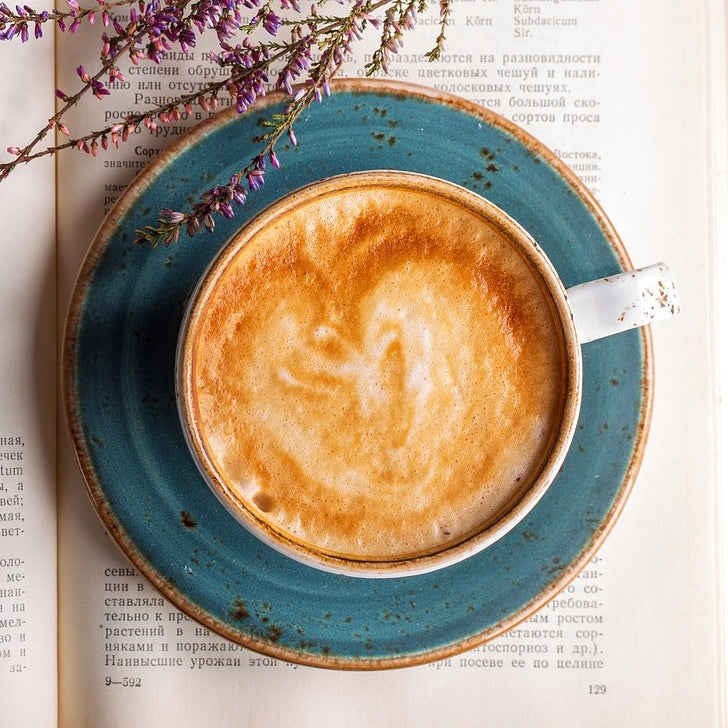 A latte on top of a book. This cup of coffee might have honey in it.