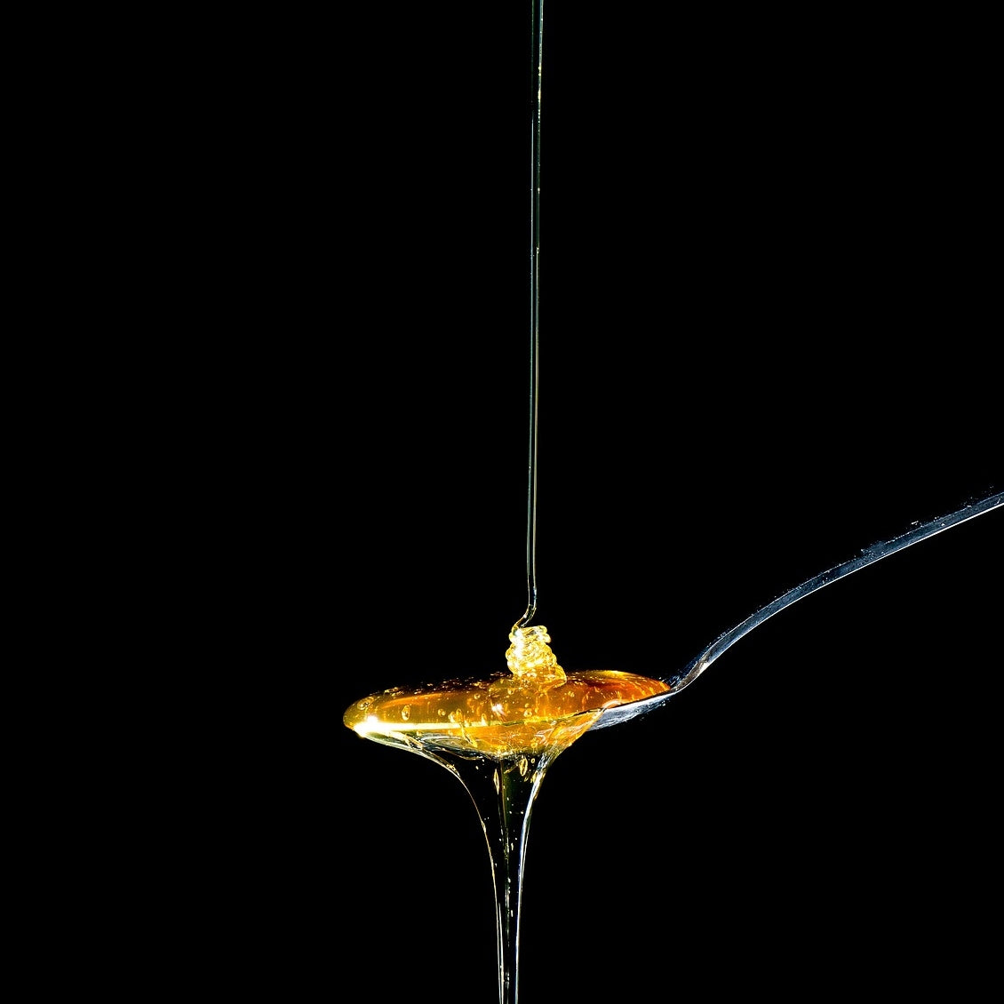 Honey being drizzled onto a spoon with a black background.