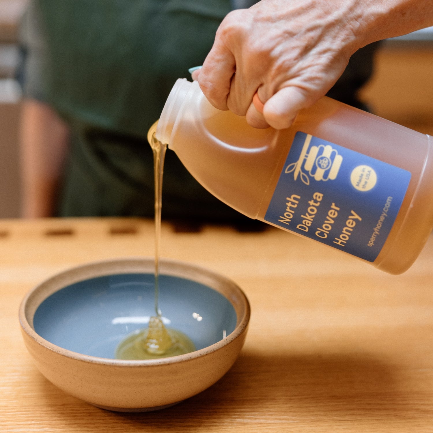A bottle of gluten free honey being poured into a bowl.