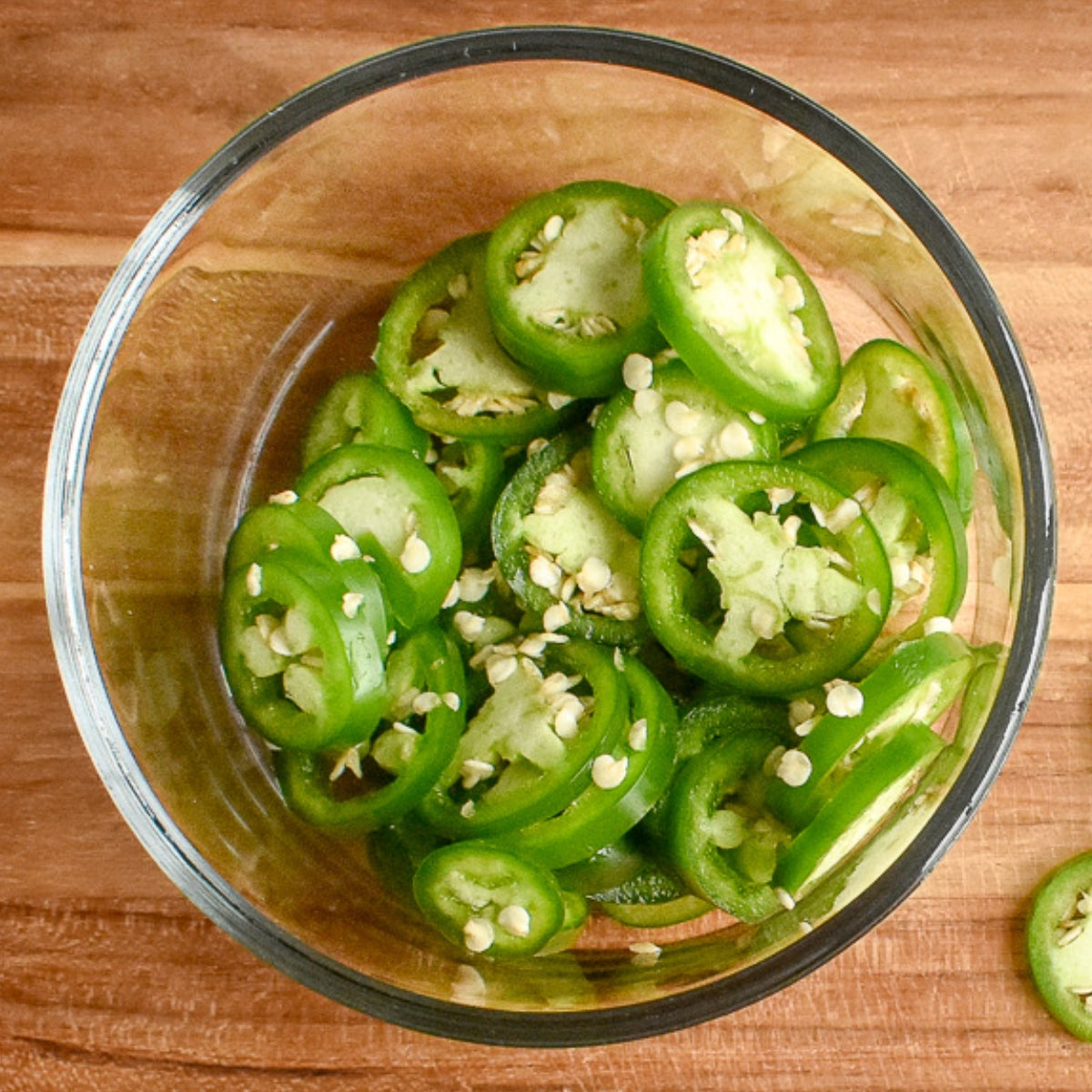 Jalapeño peppers in a glass jar on a cutting board.