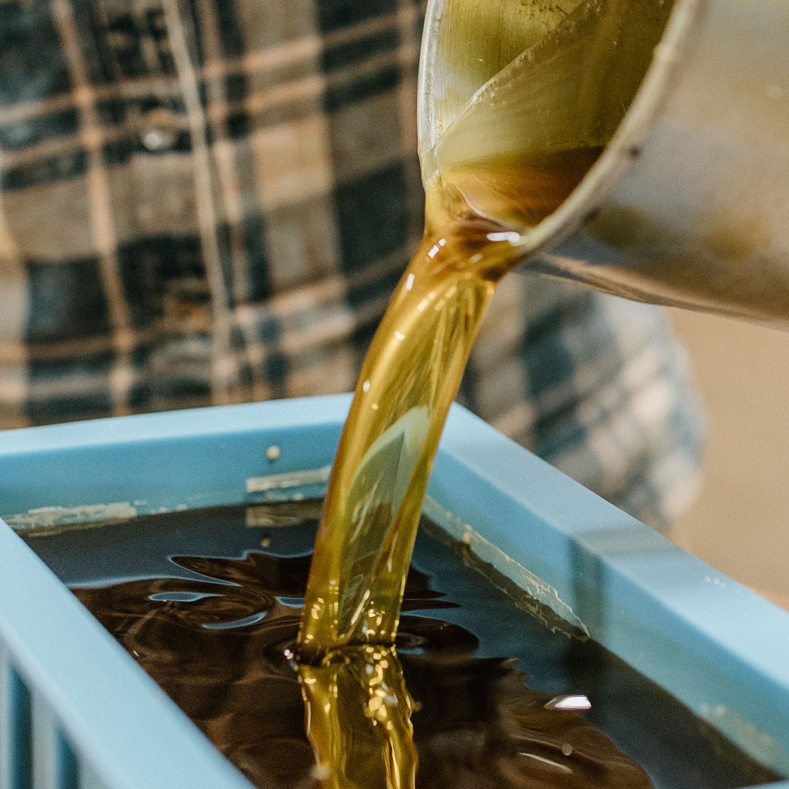 Melted beeswax being poured from a container into a blue mold.