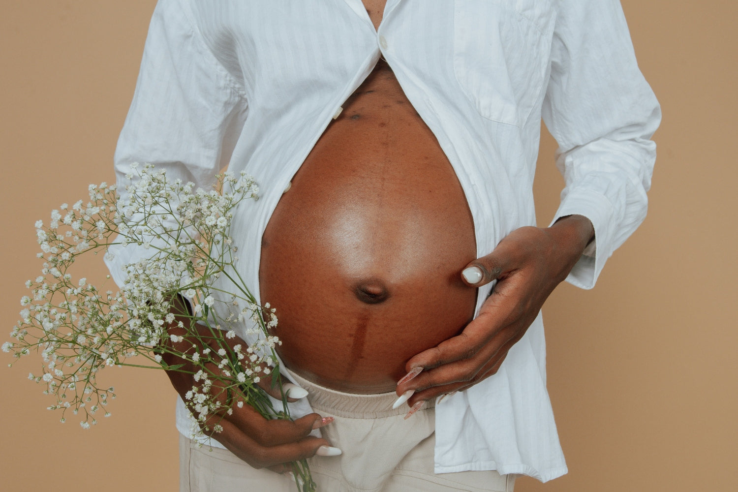 Pregnant woman holding flower and her belly.