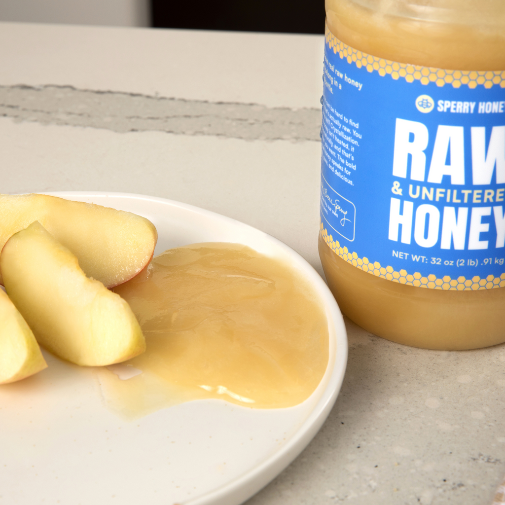 Sperry Raw Honey jar with honey on a plate of apples on a light surface