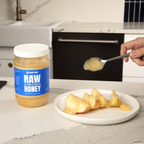 Person spooning honey onto apples with a jar of honey labeled 'Raw & Unfiltered Honey' in the background.