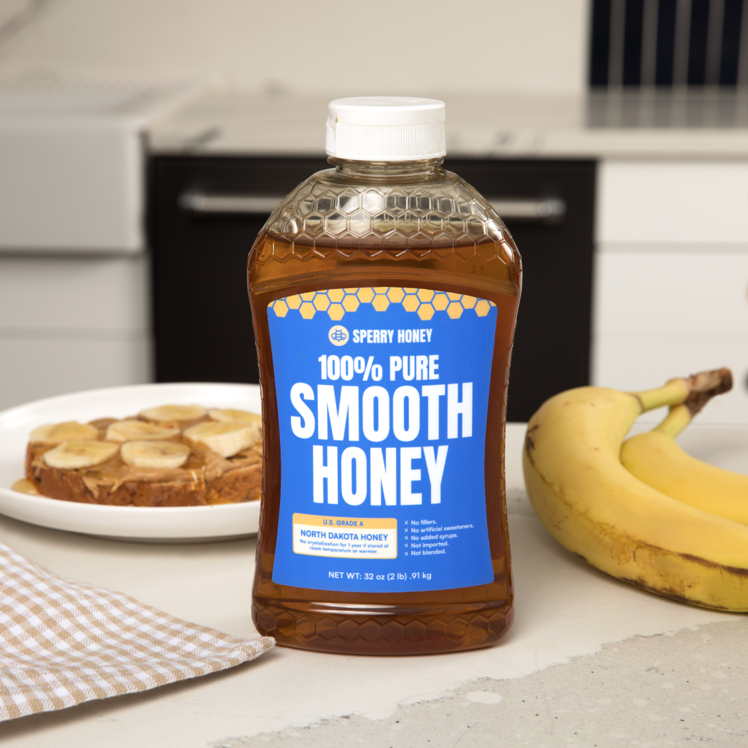 Bottle of Sperry Honey 100% Pure Smooth Honey on a kitchen counter with bananas and a cake.
