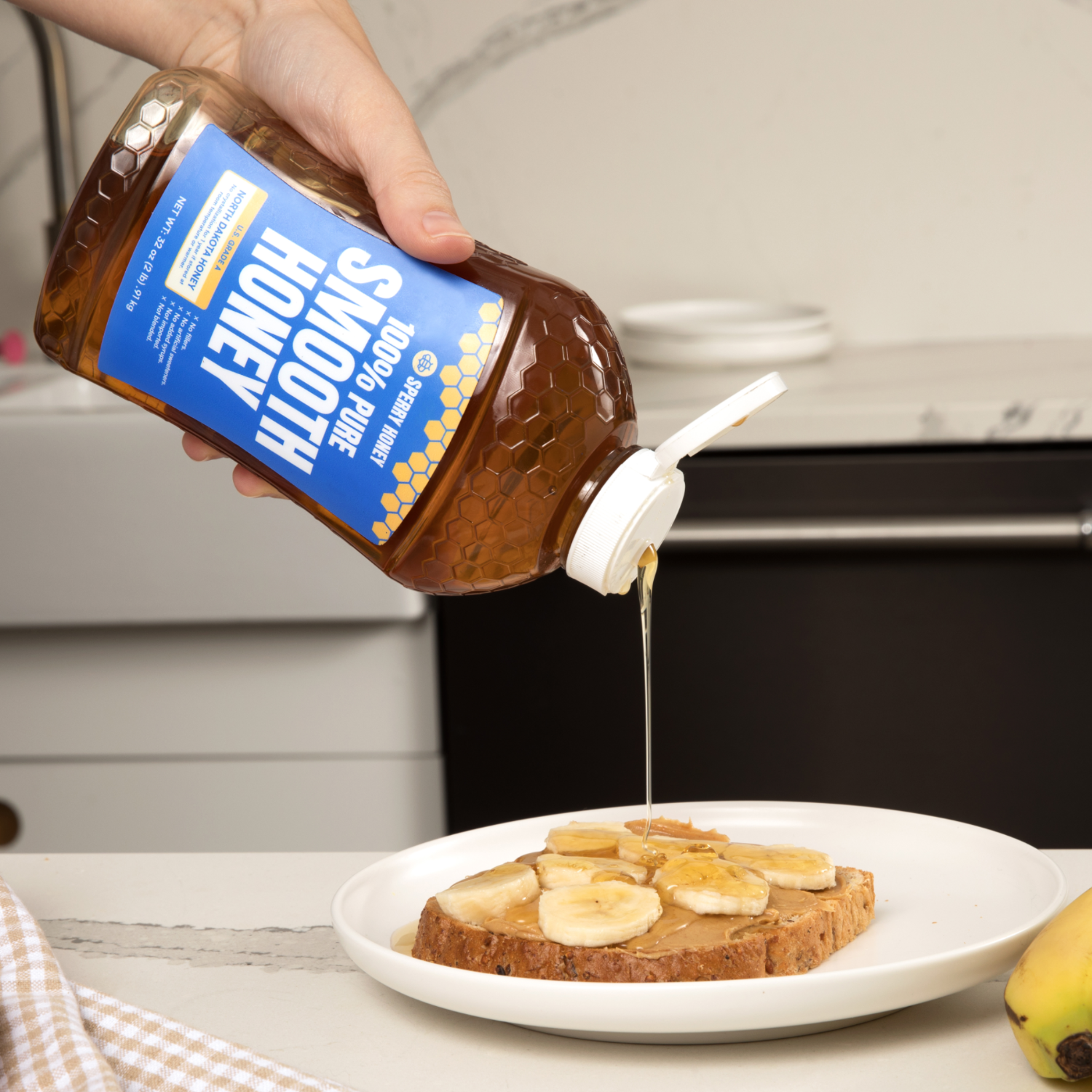 Person pouring honey from a bottle onto a plate of toast with bananas in a kitchen setting.