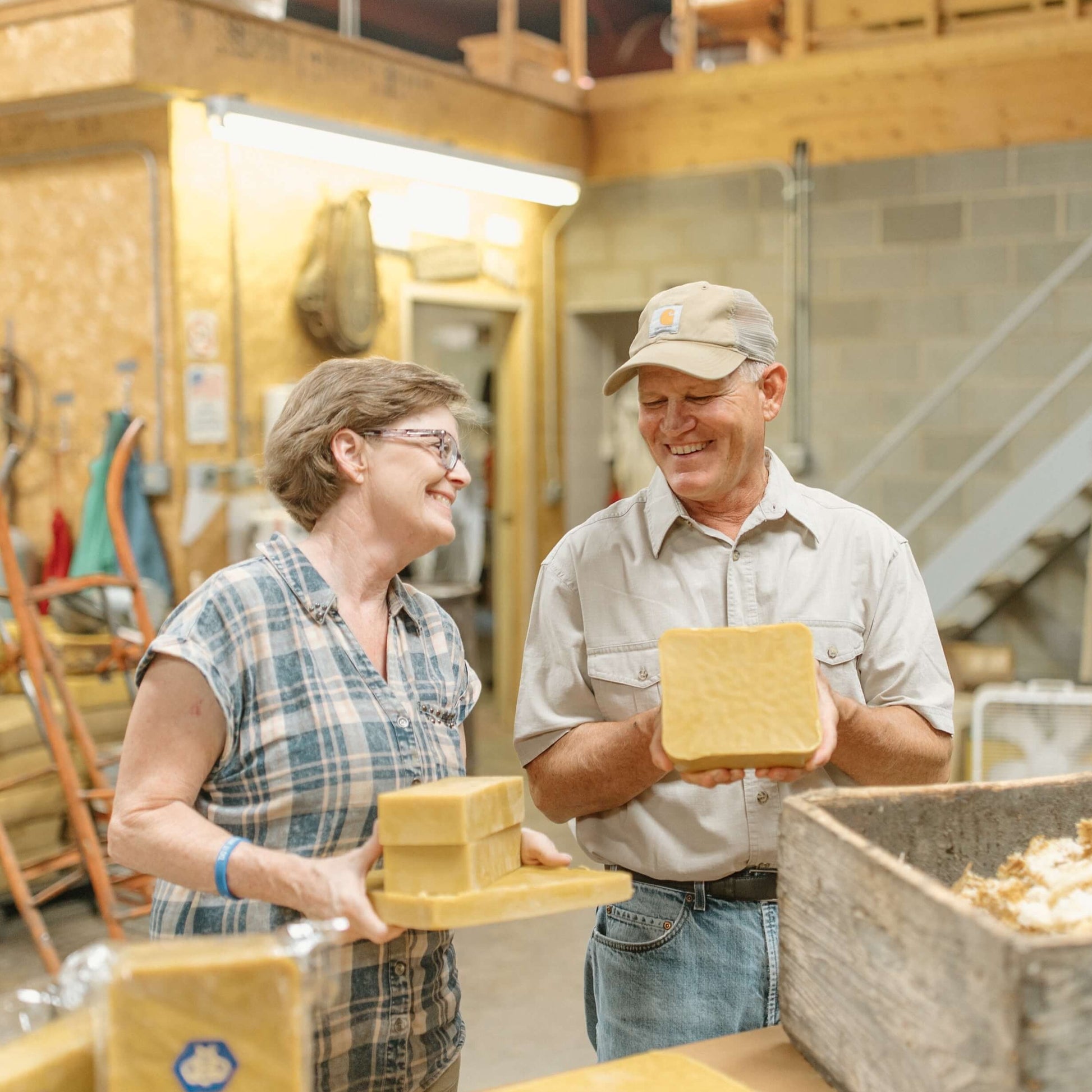 Mark and Rebecca Sperry smiling, holding a bulk quantity of yellow beeswax blocks.